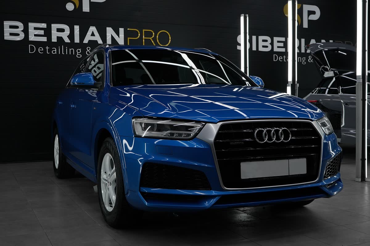 Синяя Audi Q3 перед стеной с логотипом