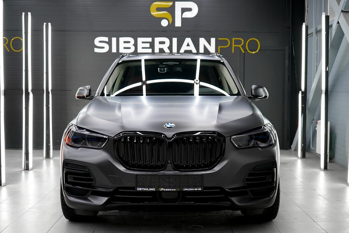 Матовый BMW X5 перед стеной с логотипом